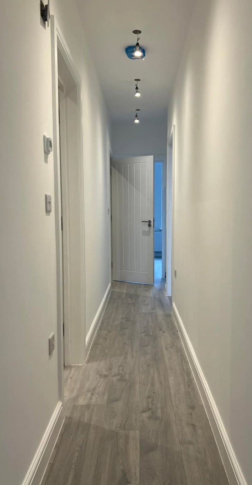 White hallway with pendant lights and wood-effect flooring